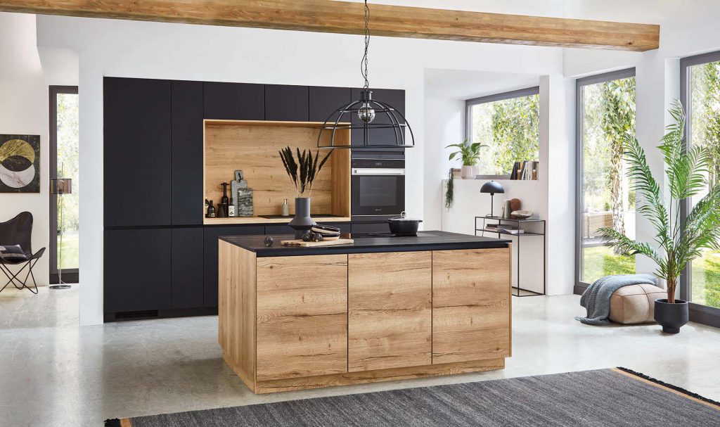 Keukentrend 2023: een matzwarte keuken met natuurlijk houten fronten en details met als opstelling een kastenwand met nis en kookeiland.